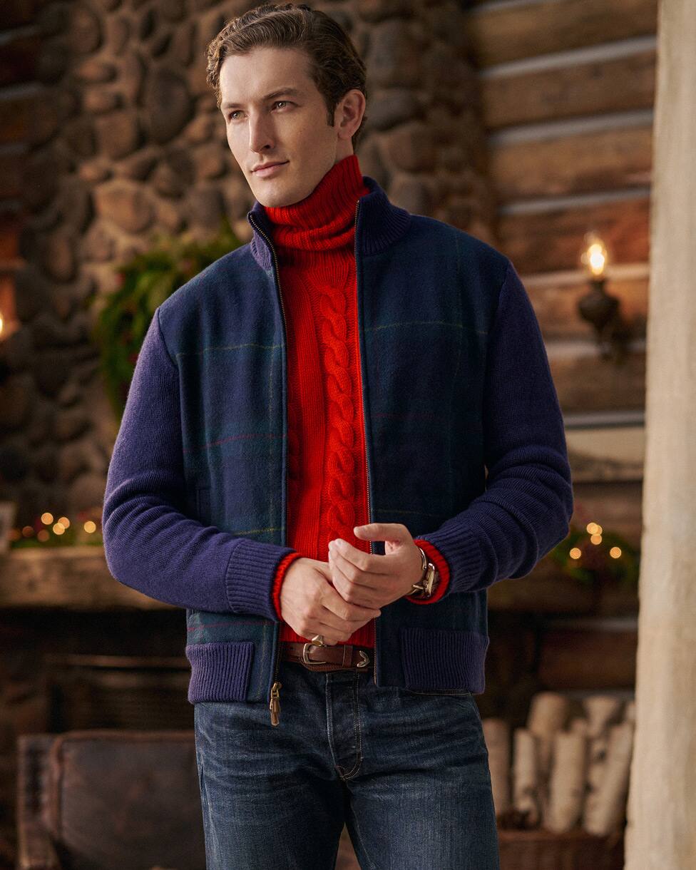 Mann in rotem Rollkragenpullover mit Zopfmuster, marineblauer Jacke und Jeans.