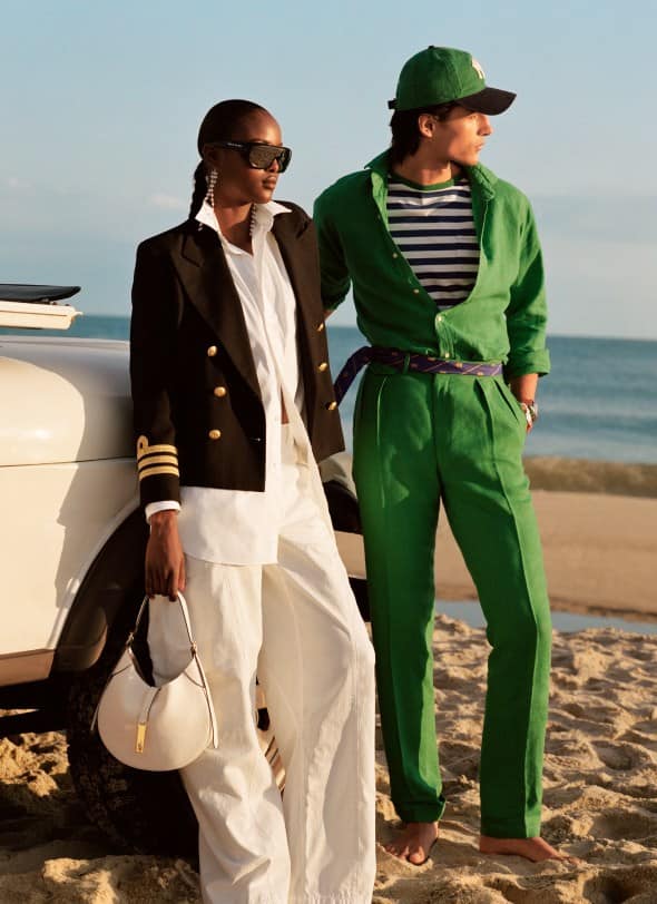 Woman and man on beach wear navy blazer over white outfit and green button-down and green trousers.